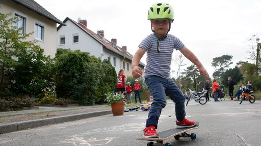Ein 4-jähriger Junge fährt mit einem Skateboard auf der temporären Spielstrasse