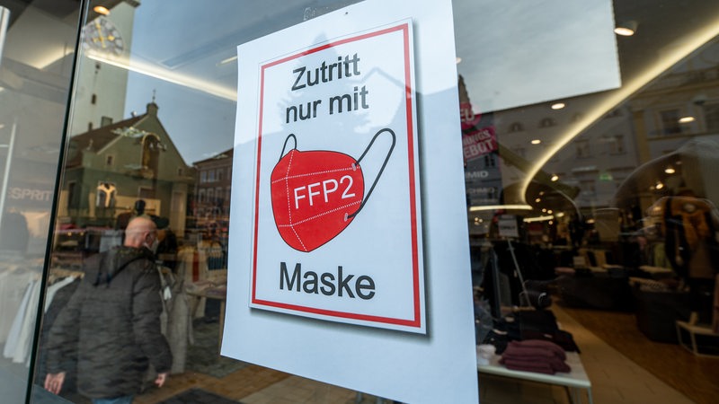 An einer Schaufensterscheibe eines Geschäfts hängt ein Hinweis auf die FFP2-Maskenpflicht.