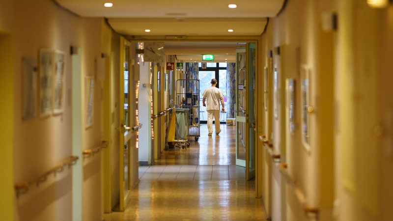 Ein Pfleger geht einen Gang eines Alten- und Pflegeheims entlang.