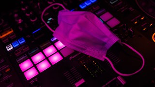 Ein Mund-Nasen-Schutz liegt auf dem Mischpult des DJs in einem Club. 