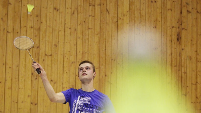 Ein junger Mann spielt in einer Halle Badminton.