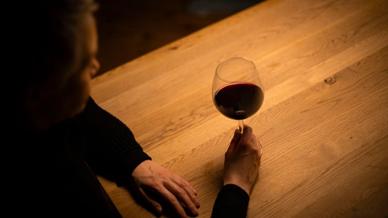 Eine Frau sitzt mit einem Glas Rotwein an einem Tisch.