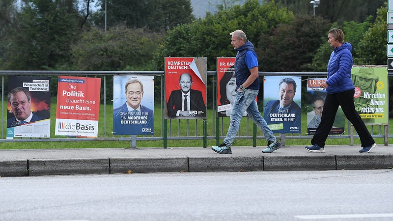 Zwei Spaziergänger gehen auf einer Brücke an einer Reihe von Wahlplakaten vorbei