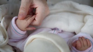 Die Hand eines Erwachsenen greift nach der Hand eines Babys