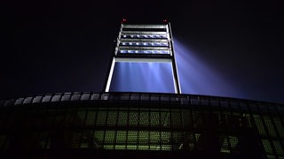 Ein Flutlichtmast des Weser-Stadions strahlt im Dunkeln.