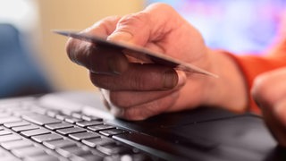 Ein Hand liegt auf einer Computertastatur und hält eine Kreditkarte