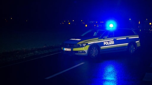 Streifenwagen der Polizei steht in Dunkelheit mit Blaulicht quer auf einer Landstraße bei einer Polizeiabsperrung.