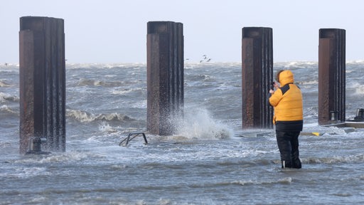 Ein Passant beobachtet, wie das Wasser der aufgepeitschten Nordsee bei Sturm den Fähranleger Dagebüll überflutet.
