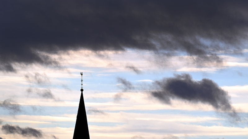 Über einen Kirchturm ziehen dunkle Wolken hinweg.