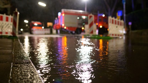 Nahe einer Einsatzstelle der Feuerwehr hat sich Regenwasser auf einer Straße angesammelt. 
