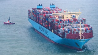 Ein Containerschiff fährt begleitet von einem Schlepper im Meer.