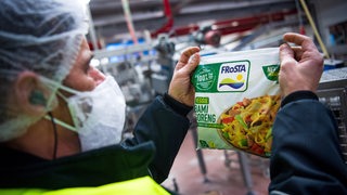 Ein Mann hält in einer Fabrik einen Tiefkühlkost-Beutel in der Hand.