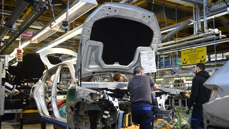 Mehrere Daimler Mitarbeiter schrauben im Bremer Mercedes-Werk an einem Auto.