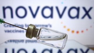 Eine Spritze, eine Impfambulle und der Schriftzug Novavax im Hintergrund