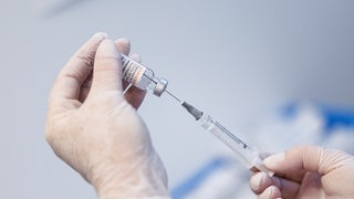 Nahaufnahme von zwei Händen, die eine Spritze mit dem Impfstoff Novavax aufziehen