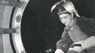 Eine Frau arbeitet mit Schutzkleidung und Schweißgerät.