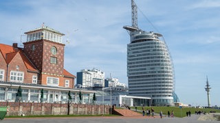 Menschen gehen vor einem Hochhaus an einem Deich spazieren.