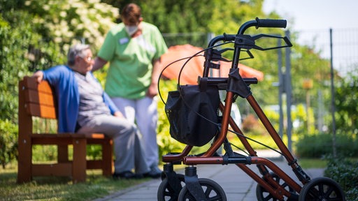 Ein Rollator steht nahe einer Pflegefachkraft und einer Bewohnerin eines Seniorenheims im Freien.