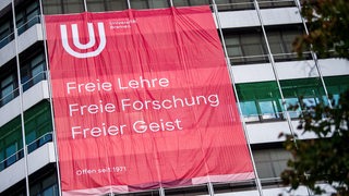 Ein Plakat mit der Aufschrift "Freie Lehre, Freie Forschung, Freier Geist" hängt an einem Gebäude der Universität Bremen. 