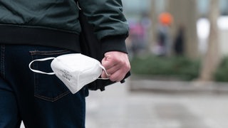Ein Mann trägt auf einer Einkaufsstraße eine FFP-2-Maske in der Hand. 