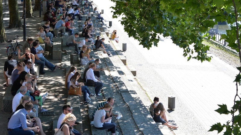 Zahlreiche Menschen sitzen in Bremen an der Schlachte und genießen ihre Mittagspause im Schatten.