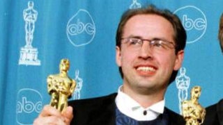 Ein Mann im Anzug hält eine goldene Trophäen in die Kamera.