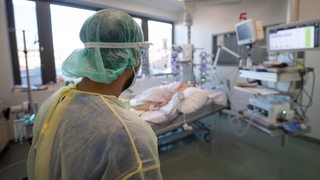 Ein Pfleger steht auf der Intensivstation für Corona-Patienten am Sana Klinikum Offenbach an einem ECMO-Bett, in dem ein Patient liegt.
