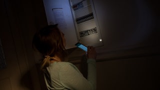 Eine Frau überprüft den Sicherungskasen bei einem Stromausfall.