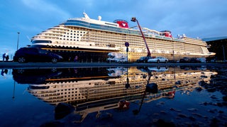 Das Kreuzfahrtschiff „Disney Wish“ wird von Schleppern aus dem Baudock der Meyer Werft gezogen und spiegelt sich dabei in einer großen Pfütze.
