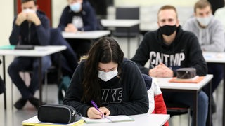 Mehrere Schüler mit Masken schreiben eine Prüfung.