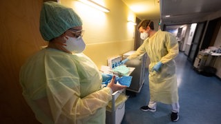 Eine Krankenpflegerin und ein Arzt legen Corona-Schutzkleidung an.