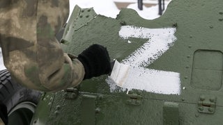 Ein russischer Soldat mal ein weißes Z auf ein Armeefahrzeug