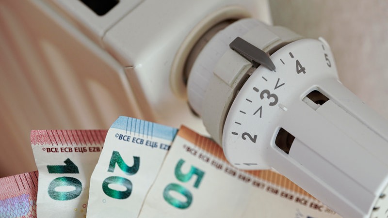 An einem Thermostatventil einer Heizung liegen verschiedene Geldscheine