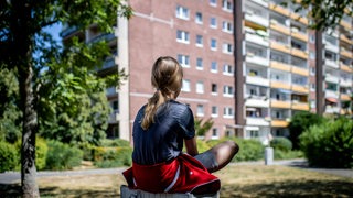 Ein Mädchen sitzt vor einem Plattenbau