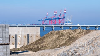 Der Jade-Weser-Port ist hinter einer Baustelle am Deich zu sehen.