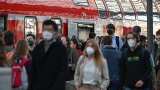 Viele Reisende am Bahnhof, im Hintergrund ein Regionalzug