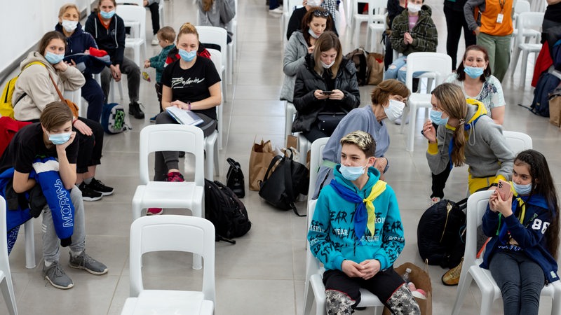 Vorwiegend junge Geflüchtete aus der Ukraine sitzen in einer Halle auf weißen Plastikstühlen