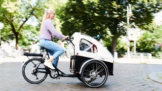 Eine Frau fährt mit einem Lasten-Fahrrad auf einem Radweg. 