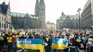 Zahlreiche Menschen haben sich während einer Kundgebung gegen den Krieg in der Ukraine hinter dem Transparent "We stand with Ukraine" auf dem Domshof versammelt.