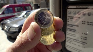Münzen in einer Hand vor einem Ticketautomaten.
