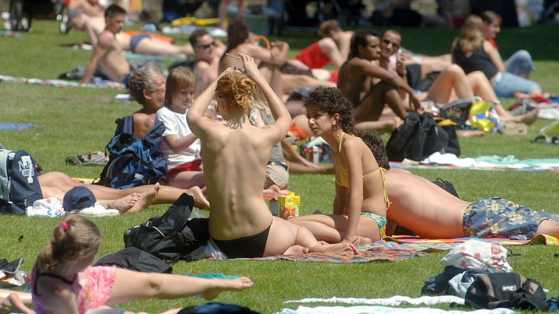 Frauen sonnen sich in einem Freibad, eine trägt dabei kein Bikini-Oberteil.