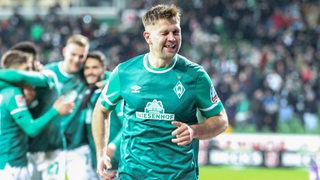 Werder-Stürmer Niclas Füllkrug zwinkert beim Torjubel kess in die Kamera und lässt dabei seine Zahnlücke aufblitzen.