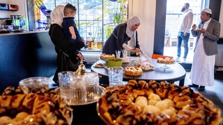 Viele süße Speisen. Dahinter Menschen mit Kopfbedeckung.