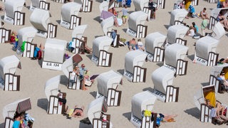 Menschen liegen zwischen Strandkörben am Strand.