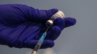 Eine Hand zieht eine Spritze mit Corona-Impfstoff auf