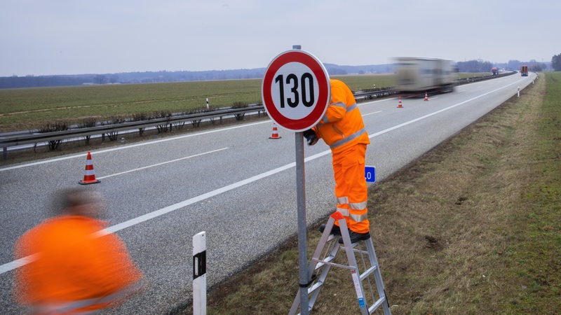Straßenwärter montieren an einer Autobahn ein Verkehrsschild mit der Geschwindigkeitsangabe 130 Stundenkilometer