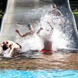 Schüler rutschen auf einer breiten Rutsche ins Schwimmbecken des Freibads Grünhöfe in Bremerhaven
