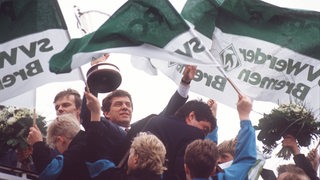 Otto Rehhagel hält 1992 den Europapokal der Pokalsieger hoch. Um ihn herum werden Werder-Fahnen geschwenkt.