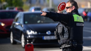 Ein Polizist winkt bei einer Verkehrskontrolle ein Auto an den Straßenrand.