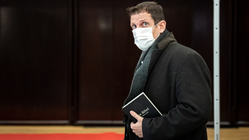 Ein Mann mit einer OP-Maske trägt eine Bibel unter dem Arm.